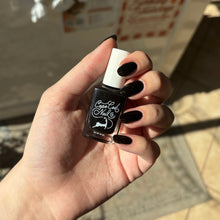 Load image into Gallery viewer, A hand holding a bottle of black nail polish, with the nails painted in a glossy black finish. The bottle has a white cap and a black label with white script reading 'Cape Cod Nail Co'.
